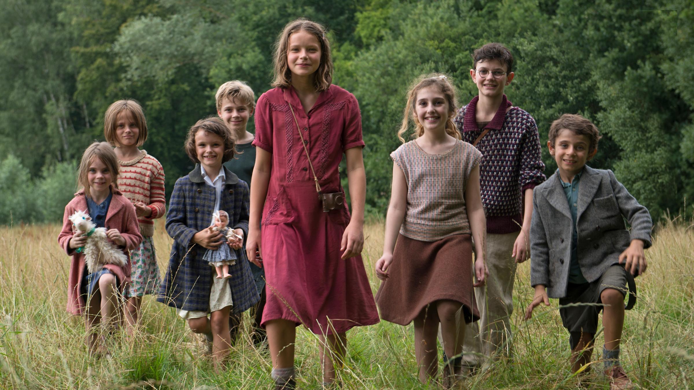 Fannys Reise: Fanny (Léonie Souchaud, 4.v.r.) läuft mit einer Gruppe von sieben Kindern über eine Wiese. Sie versucht, diese aus ddem besetzten Frankreich herauszubringen. Im Hintergrund ein Wald.