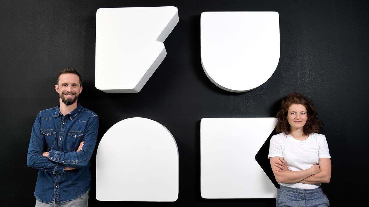 Florian Hager (r.; Geschäftsführer funk) und Sophie Burkhardt (l.; stellvertretende Geschäftsführerin funk) vor dem funk-Logo