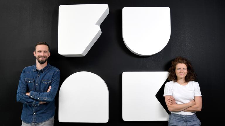 Florian Hager (r.; Geschäftsführer funk) und Sophie Burkhardt (l.; stellvertretende Geschäftsführerin funk) vor dem funk-Logo