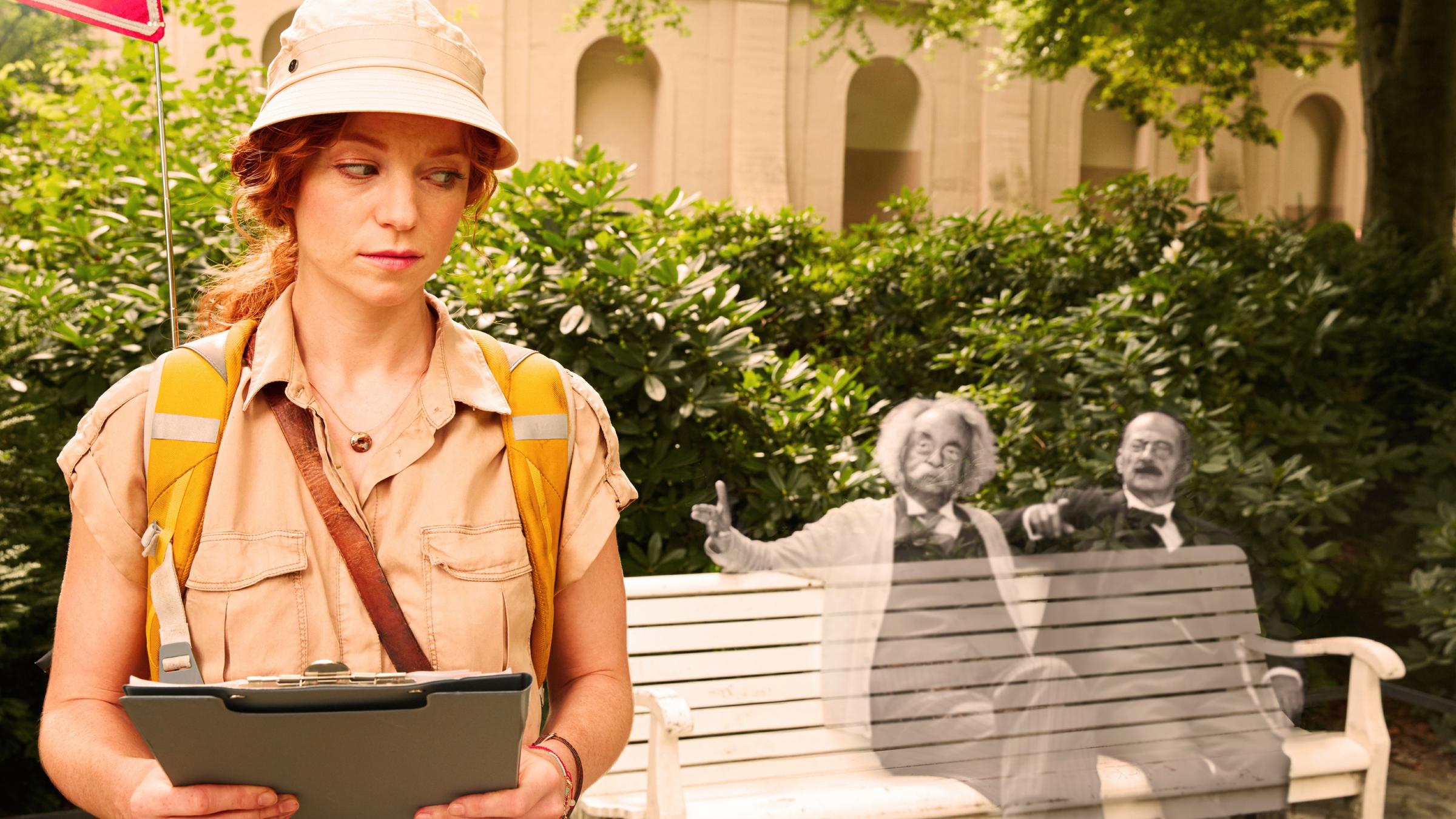 Stadtführerin Cleo (Marleen Lohse) steht vor einer Bank, auf der - in Schwarzweiß -  Albert Einstein (Jean Pütz) und Max Planck (Peter Meinhardt) sitzen und nur von ihr gesehen werden.