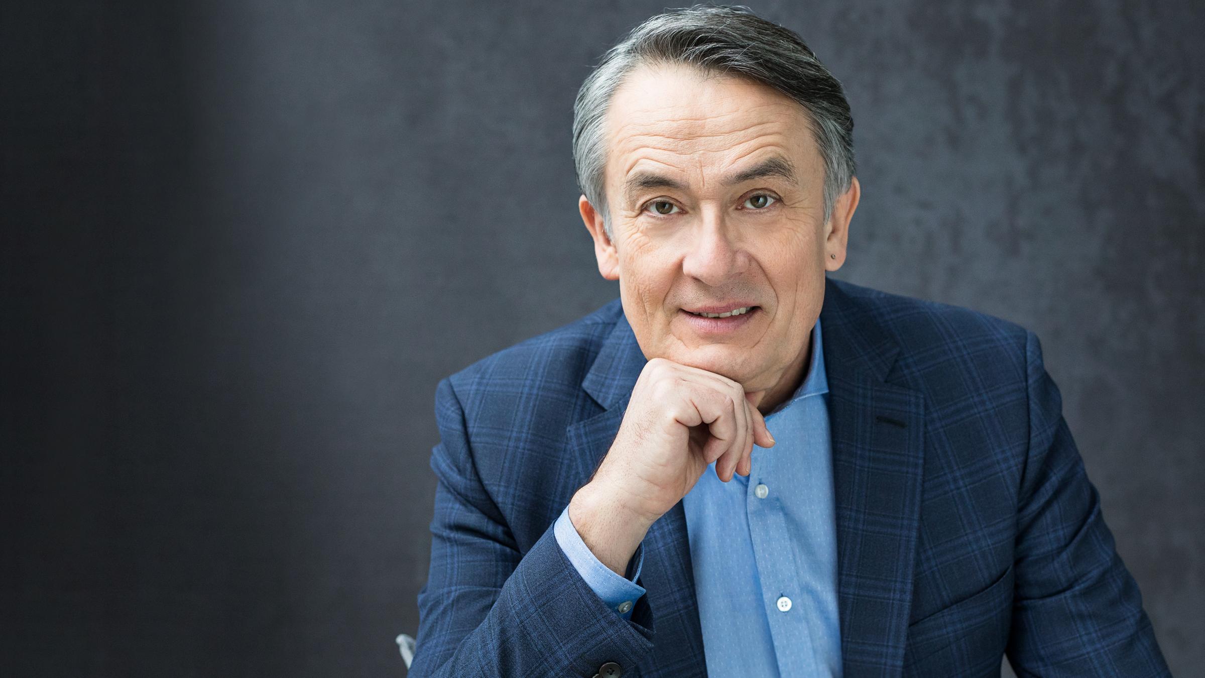 "Gert Scobel": Porträtbild von Gert Scobel (nur Oberkörper). Er trägt ein hellblaues Hemd und ein blaukariertes Sakko. Er schaut lächelnd in die Kamera