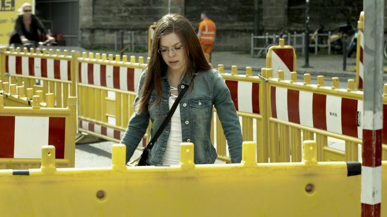 Ab 18! - See you (3sat): Eine junge Frau läuft zwischen Baustellebasperrungen durch. Im Hintergrund eine Straße.