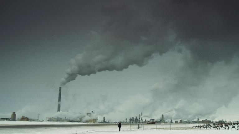 "Dark Eden": Riesige Industrieanlage mit Schloten, in der Mitte des Bildes ganz kleine eine junge Frau.