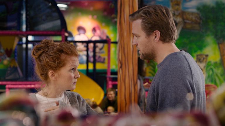 "The Love Europe Project": Eine Frau und ein Mann (Janne Heltberg und Tobias Santelmann) stehen sich in einem bunt dekorierten Raum gegenüber und schauen sich streitlustig an.