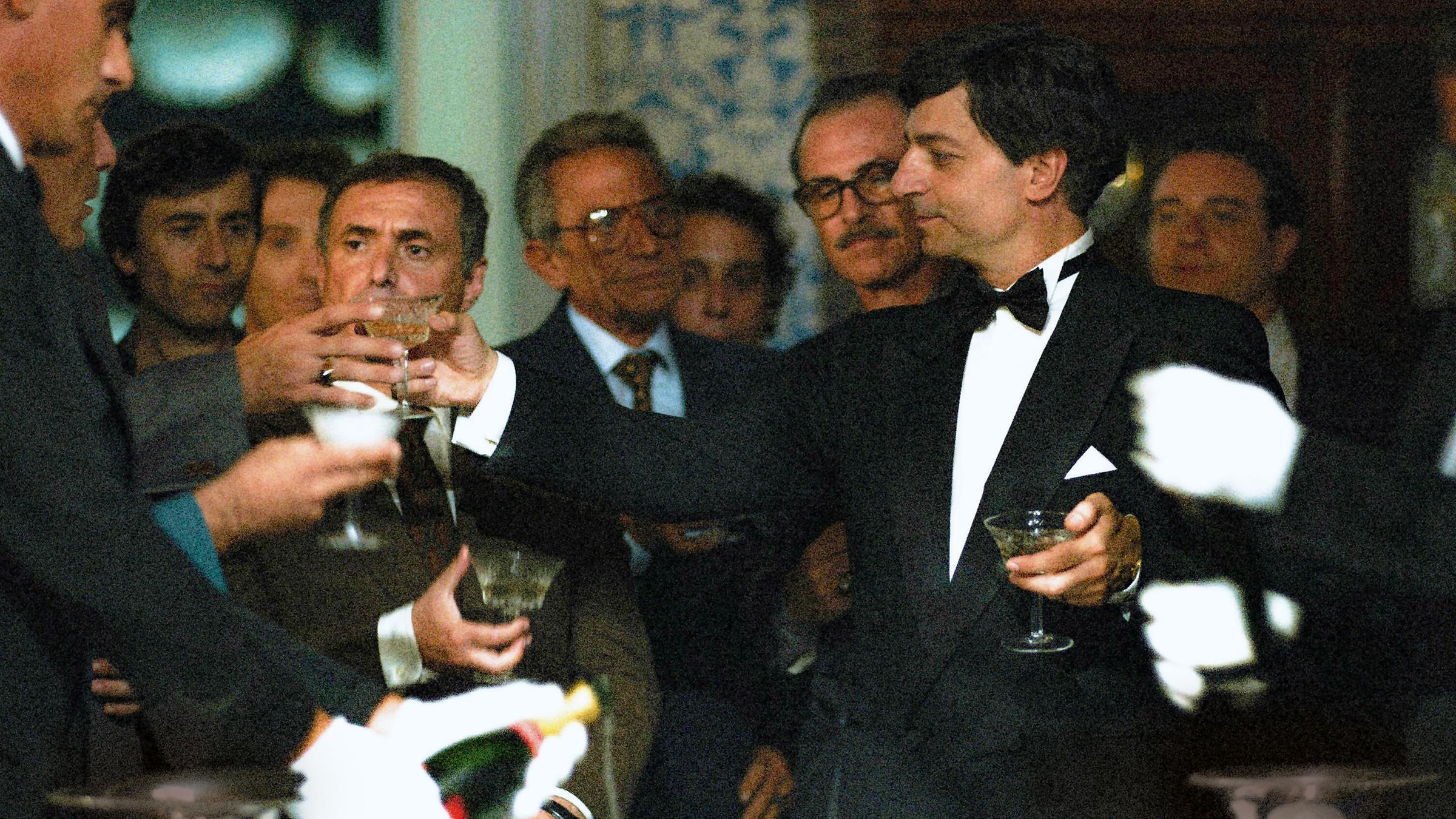 "Il Traditore": Mitglieder einer Mafia-Organisation in eleganten Anzügen stehen zusammen und stoßen mit Champagner an.