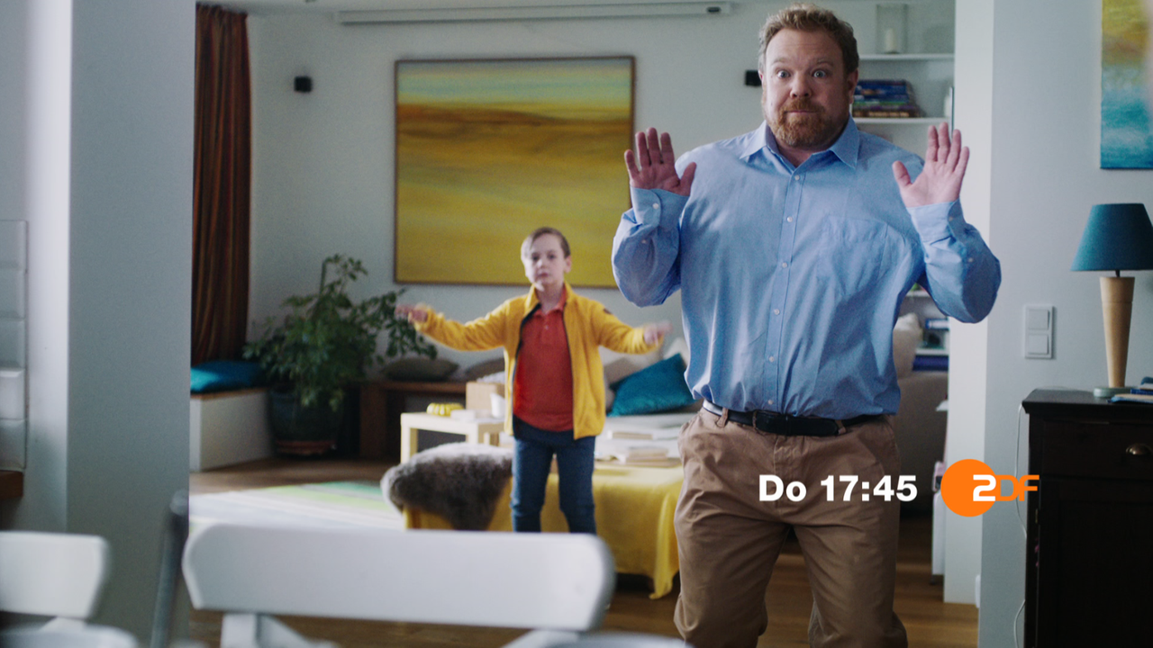 Screenshot Trailer Handball-EM 2020: Ein Mann und hinter ihm ein kleiner Junge stehen im Wohnzimmer und ahmen die Bewegung eines ballwerfenden Handballers nach.