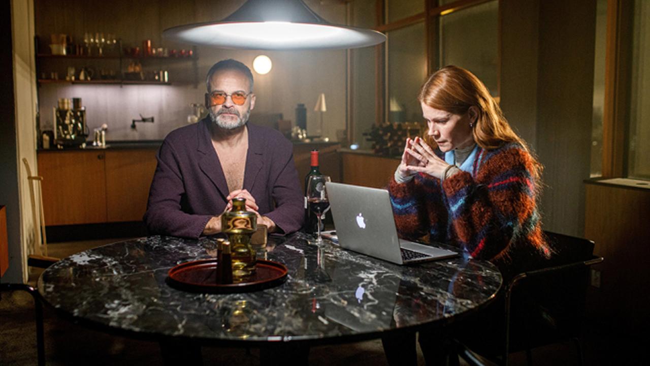 "Agatha Christie's Sven Hjerson": Sven Hjerson (Johan Rheborg)  und die TV–Produzentin Klara Sandberg (Hanna Alström) sitzen in einer Wohnung an einem runden Tisch. Sven trägt eine orange getönte Brille und schaut in die Kamera. Klara hat die Hände vor dem Gesicht gefaltet und blickt konzentriert auf ihren Laptop. Im Hintergrund eine Küchenzeile.