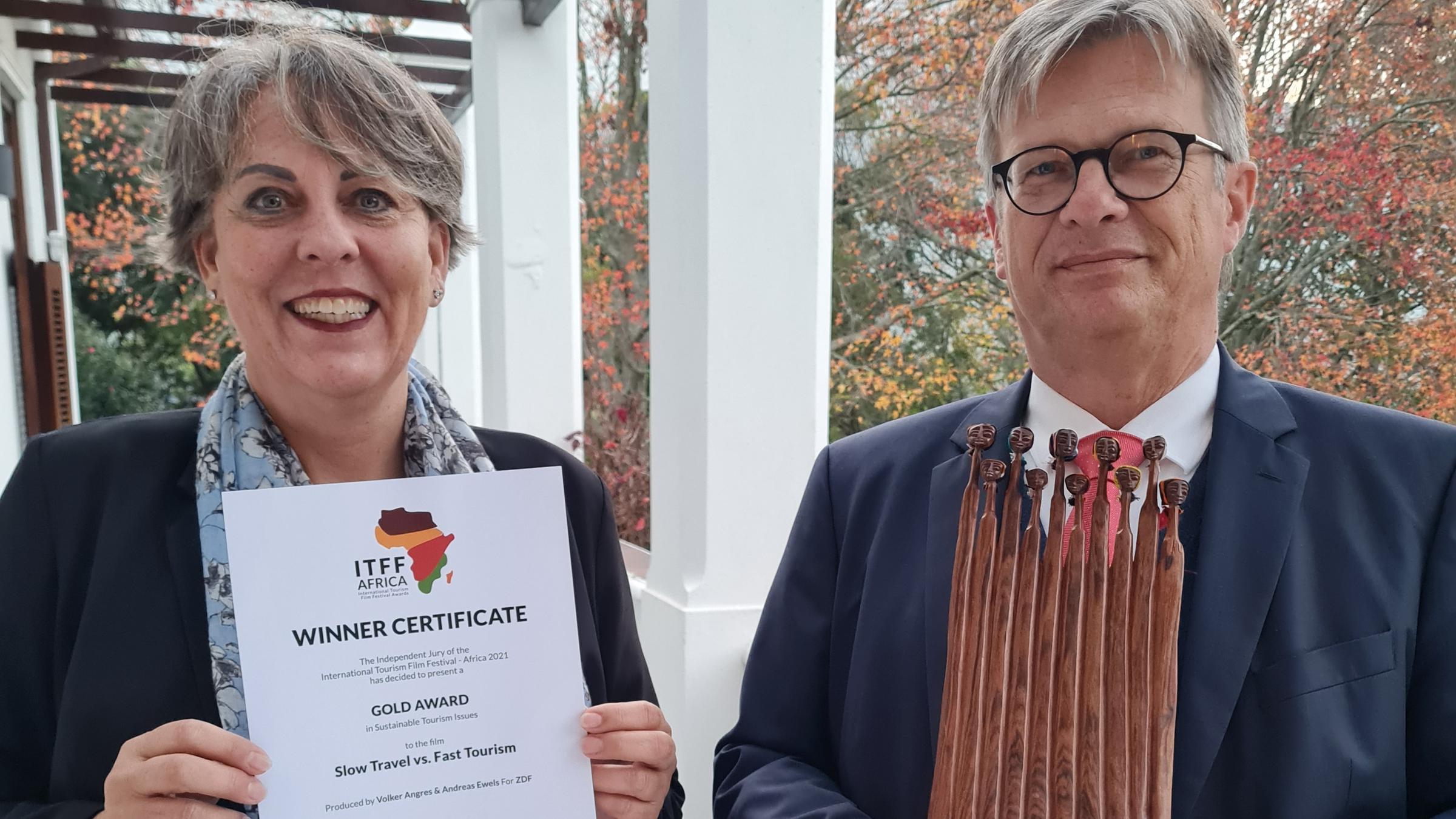 Generalkonsul Matthias Hansen und Kirsten Buchhorn (Foto) vom Auswärtigen Amt / Generalkonsulat Kapstadt präsentieren die Urkunde des Golden Award, mit dem die planet e.-Dokumentation „Reiselust, Reisefrust – Tourismus nach Corona“ auf dem ITFF in Kapstadt ausgezeichnet wurde. 