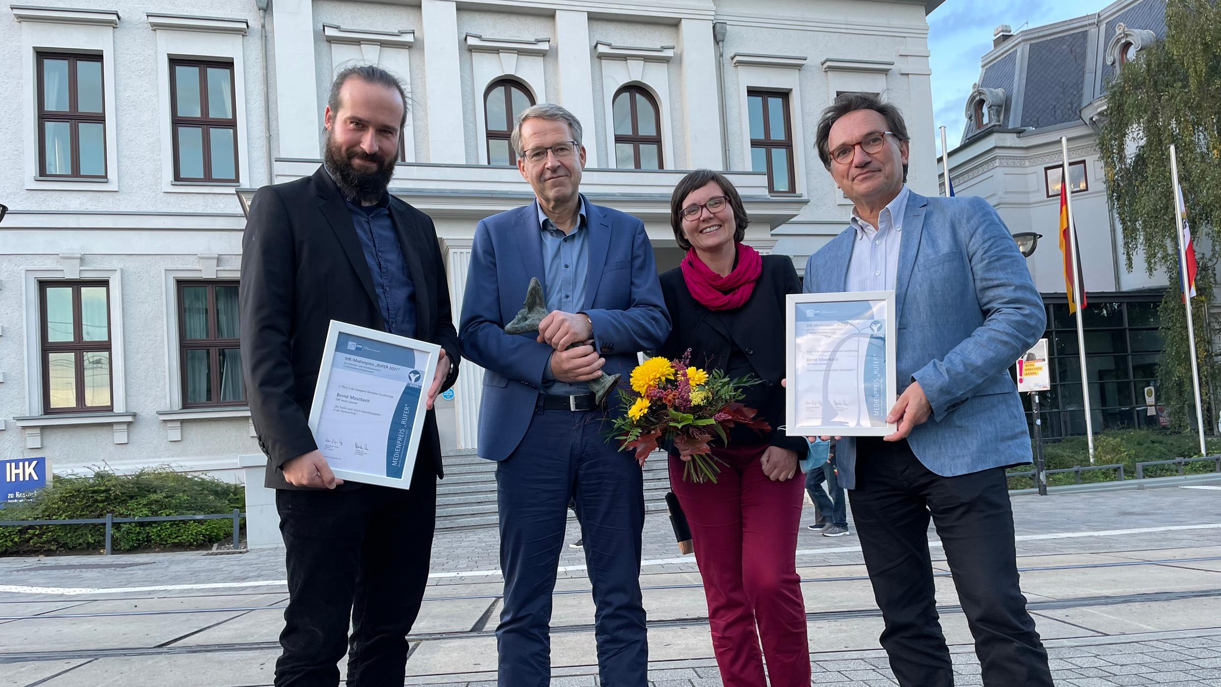 Verleihung "Rufer"-Medienpreis 2021:  v.l.: Cutter Frank Zimmermann, Studioleiter Bernd Mosebach, Anja Kapinos (Preisträgerin 2020) und Kameramann Mathias Burkardt. Im Hintergrund das IHK-Gebäude in Schwerin