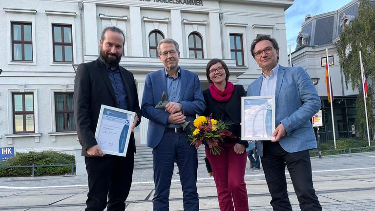 Verleihung "Rufer"-Medienpreis 2021:  v.l.: Cutter Frank Zimmermann, Studioleiter Bernd Mosebach, Anja Kapinos (Preisträgerin 2020) und Kameramann Mathias Burkardt. Im Hintergrund das IHK-Gebäude in Schwerin