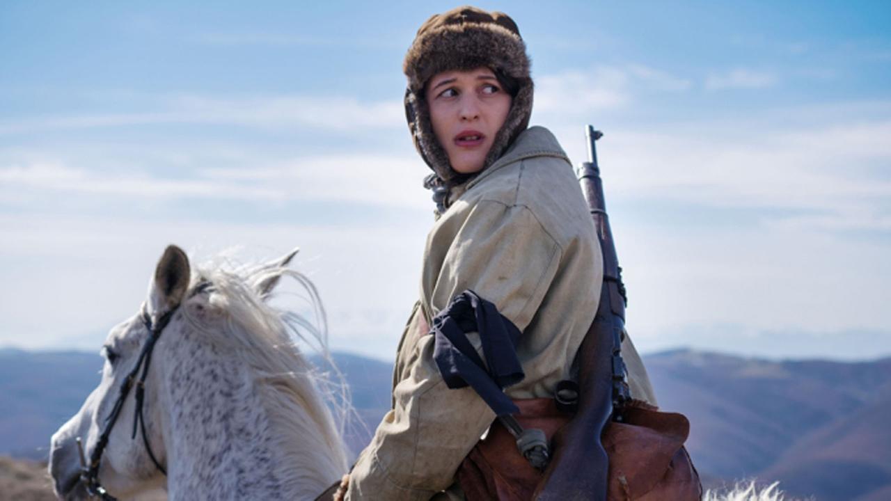 "Die albanische Jungfrau" (ZDF/ARTE): Luana (Rina Krasniqi) sitzt auf einem weißen Pferd und blickt sich mit angstvollem Blick um. Sie trägt eine Pelzmütze und auf dem Rücken ein Gewehr.