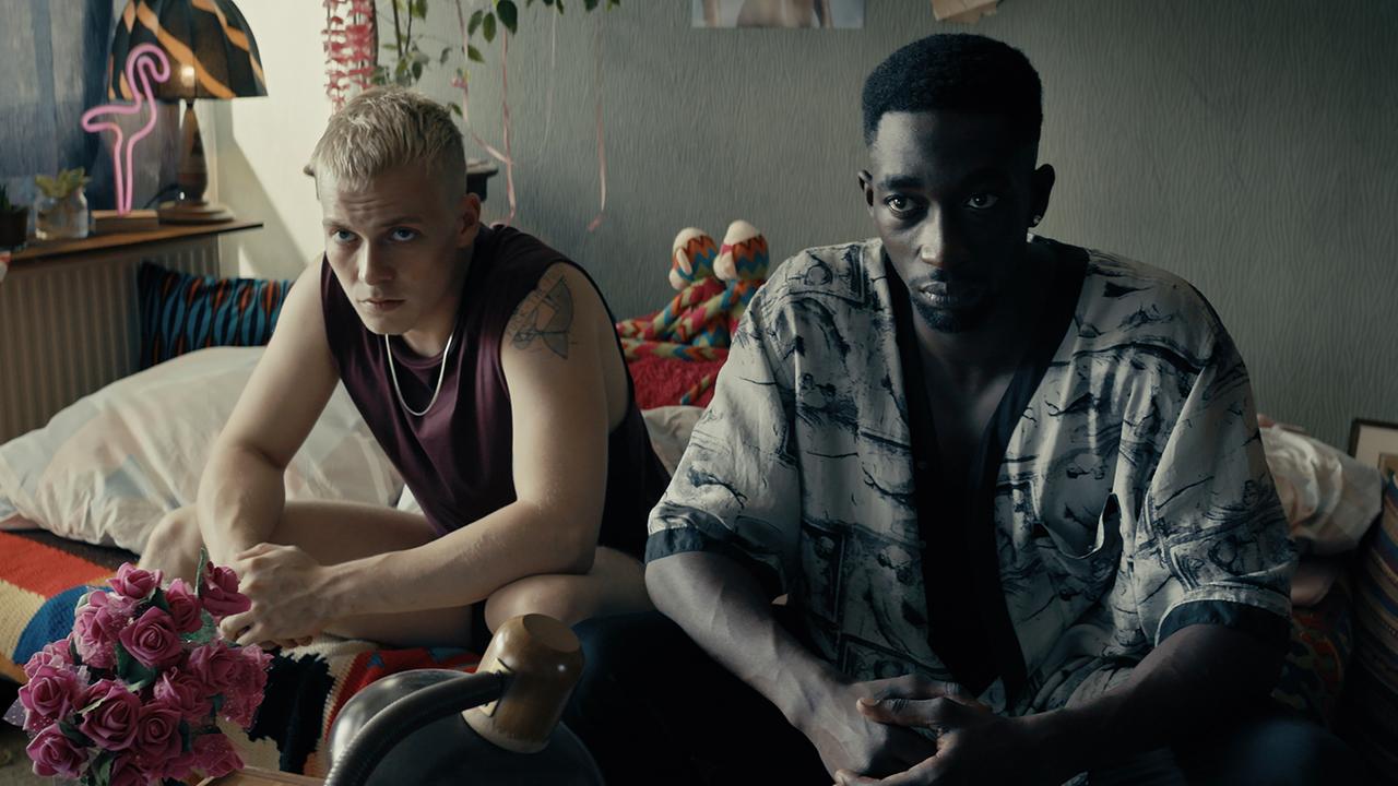 "TOUBAB": Dennis (Julius Nitschkoff)  und Babtou (Farba Dieng) sitzen nebeneinander auf einem Bett und blicken ernst in die Kamera.