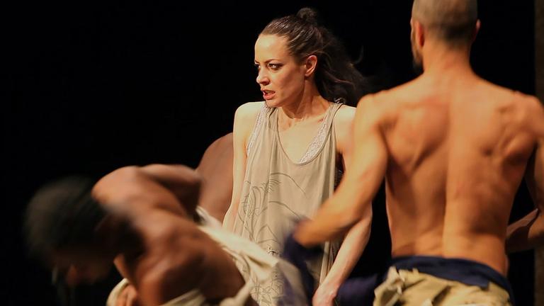 "Why we fight?": Filstill . - Zwei Männer mit nacktem Oberkörper und eine Frau kämpfen in einer Art Ringkampf