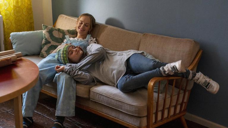 "Sweet Disaster": Frida (Friedrike Kempter) sitzt lächelnd auf einem Sofa. Neben ihr liegt Yolanda (Lena Urzendowsky) mit ihrem Kopf in Lenas Schoß. Sie hat die Augen geschlossen und eine Mütze auf em Kopf