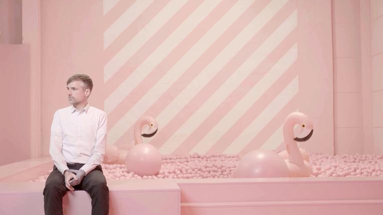 "Agree to Disagree!" (ARTE): Bertold Meyer, Professor für Arbeits- und Orgabnisationspsychologie an der TU Chemnitz, Musiker  und DJ, sitzt, nach rechts blickend, in einem komplett in Rosa gehaltenen Raum auf dem Rand eines rosa Bällebades, aus dem zwei aufblasbare Flamingos herausschauen.