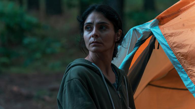 "Alaska": Eine junge Frau in Nahaufnahme steht im Wald neben einem orangefarbenen Zelt und blickt über ihre rechte Schulter zur Seite