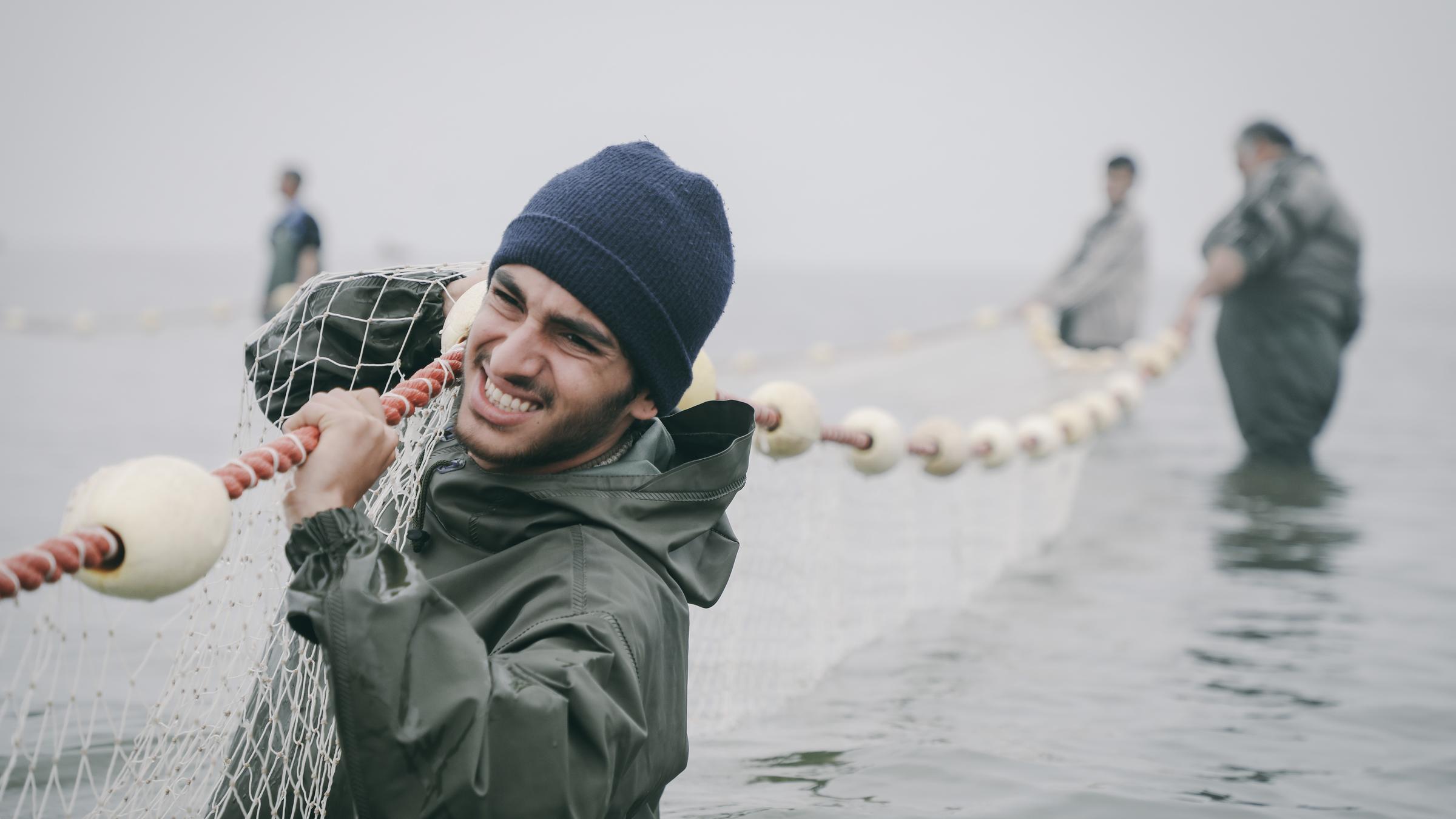 "Leere Netze": Amir (Hamid Reza Abbasi) steht im Wasser und hat ein großes Fischernetz über seine Schulter gelegt. Sein Gesicht drückt Anstrengung aus.