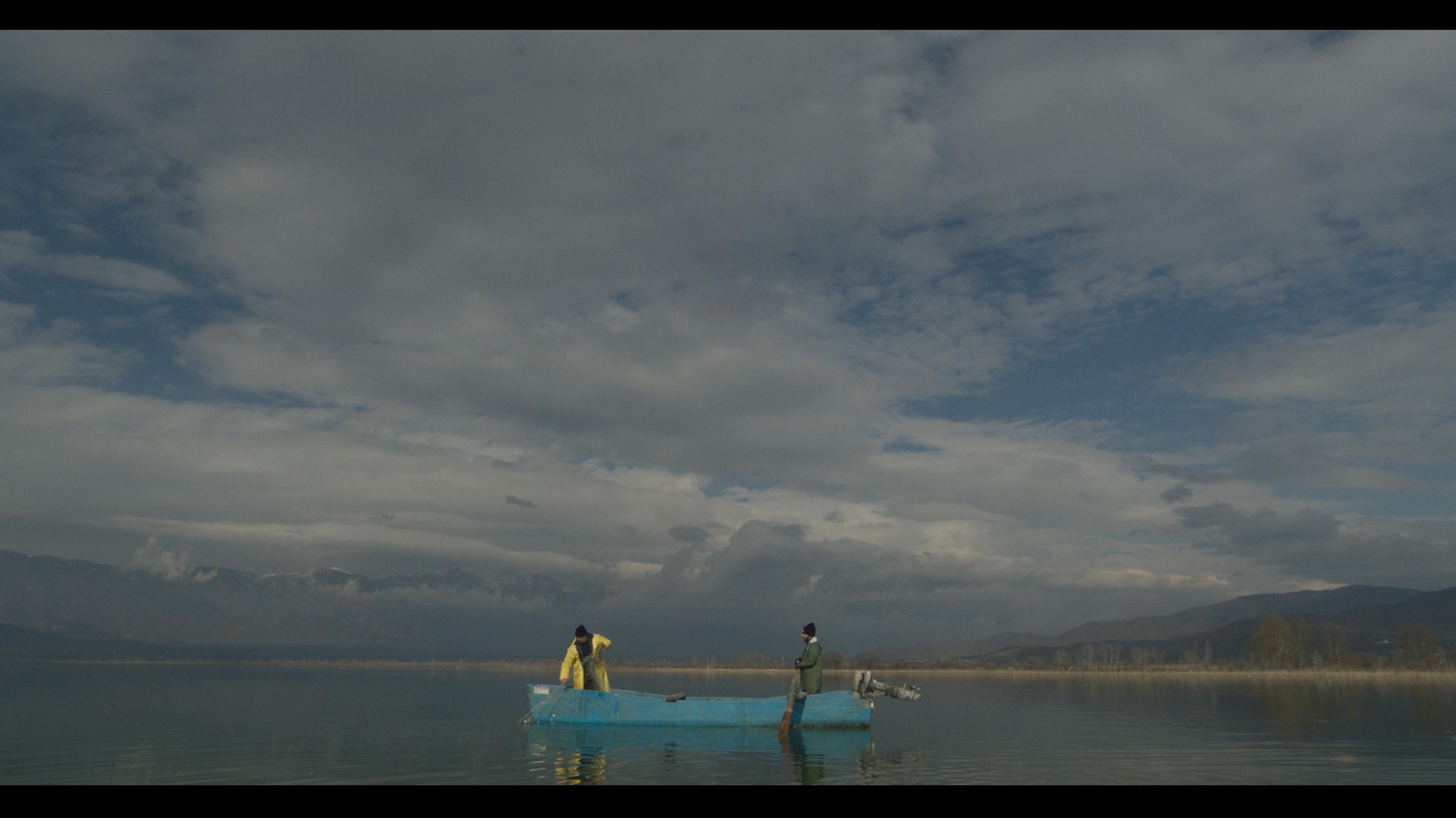 "Hinter den Fassaden" ("Behind the haystacks"): Auf einem See stehen zwei Fischer auf einem blauen Boot mit Außenbordmotor. Im Hintergrund schilfbewachsenes Ufer und Hügel am Horizont.