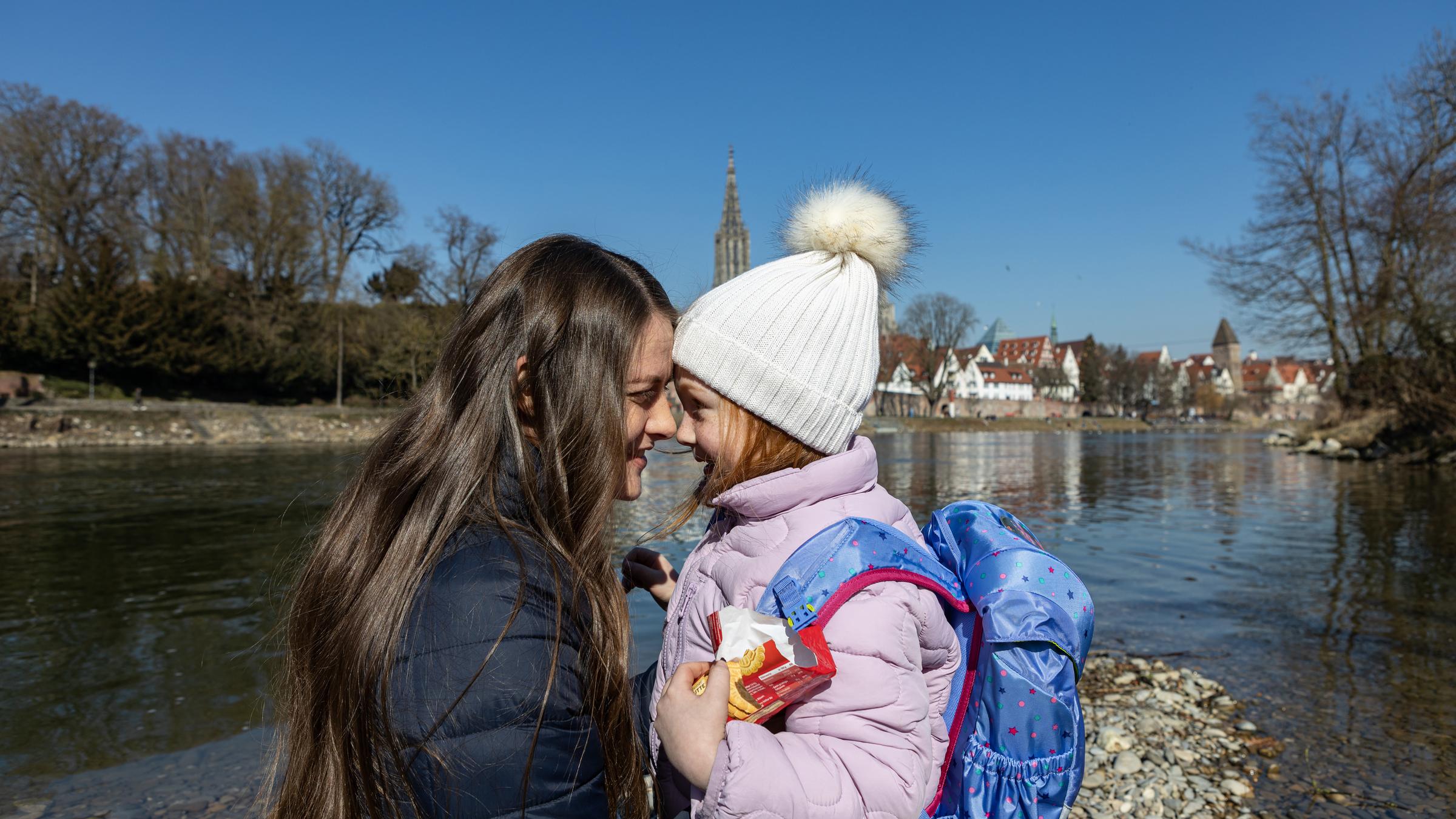 "Clara": Clara (Olga Török) und Johanna (Elina Leitl) stehen an einem Flussufer und blicken sich in die Augen. Ihre Stirnen berühren sich dabei.Johanna trägt eine weiße Pudelmütze und einen blau gemusterten Schulranzen.