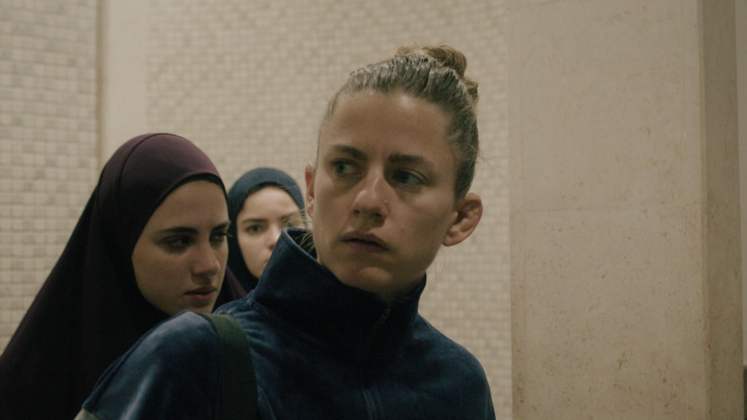 "Mond" (ARTE):  Sarah (Florentina Holzinger) blickt beunruhigt nach rechts. Im Hintergrund zwei junge Frauen in jordanischer Tracht.