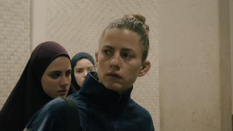 "Mond" (ARTE):  Sarah (Florentina Holzinger) blickt beunruhigt nach rechts. Im Hintergrund zwei junge Frauen in jordanischer Tracht.