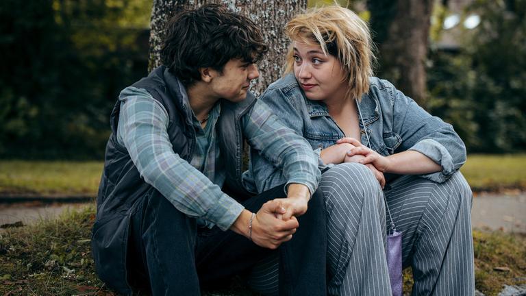 "No Dogs Allowed": Gabo (Carlo Krammling) sitzt neben seiner Schwester Emi (Bineta Hansen) unter einem Baum. Sie blicken sich gegenseitig in die Augen.