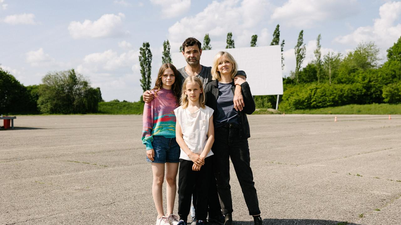 "Jupiter" - Drehstartfoto. Von links: Lea (Mariella Aumann), Paul (Henry Kofahl), Barbara (Laura Tonke), oben: Thomas (Andreas Döhler) stehen Arm in Arm auf einem großen, asphaltierten Platz. Im Hintergrund ist eine weiße Plakatwand zu sehen.