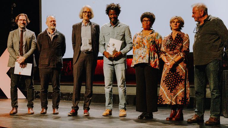 Preisverleihung "Silberne Taube" beim 67. DOK Fest Leipzig (3.11.2024): v.l.n.r.: Jurymitglieder Eric Hynes und Mark Edwards, Johannes Dicke (Leiter der Programmplanung 3sat), Preisträger Pierre Michel Jean, Jurymitglieder Sylvaine Dampierre, Maria Bonsanti und Avi Mograbi. 