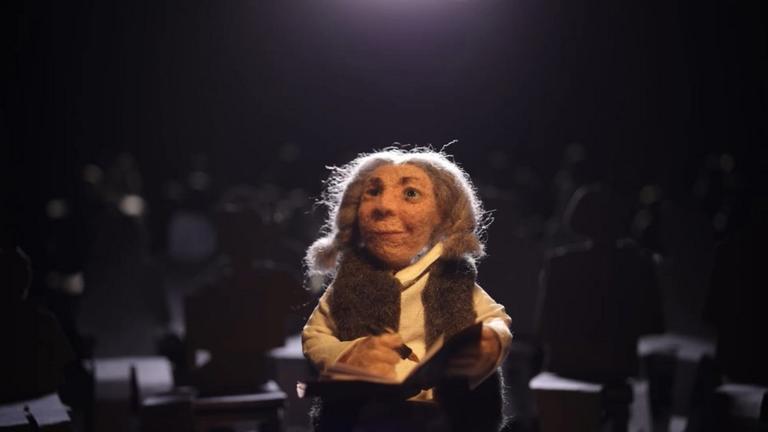 "Mama Micra": Szenenfoto; eine Puppe schreibt in ein Buch