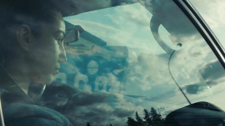 "Aïcha": Aya (Fatma Sfar) sitzt am Steuer eines fahrenden Autos. Die vorbeiziehende Landschaft spiegelt sich in der Seitenscheibe.