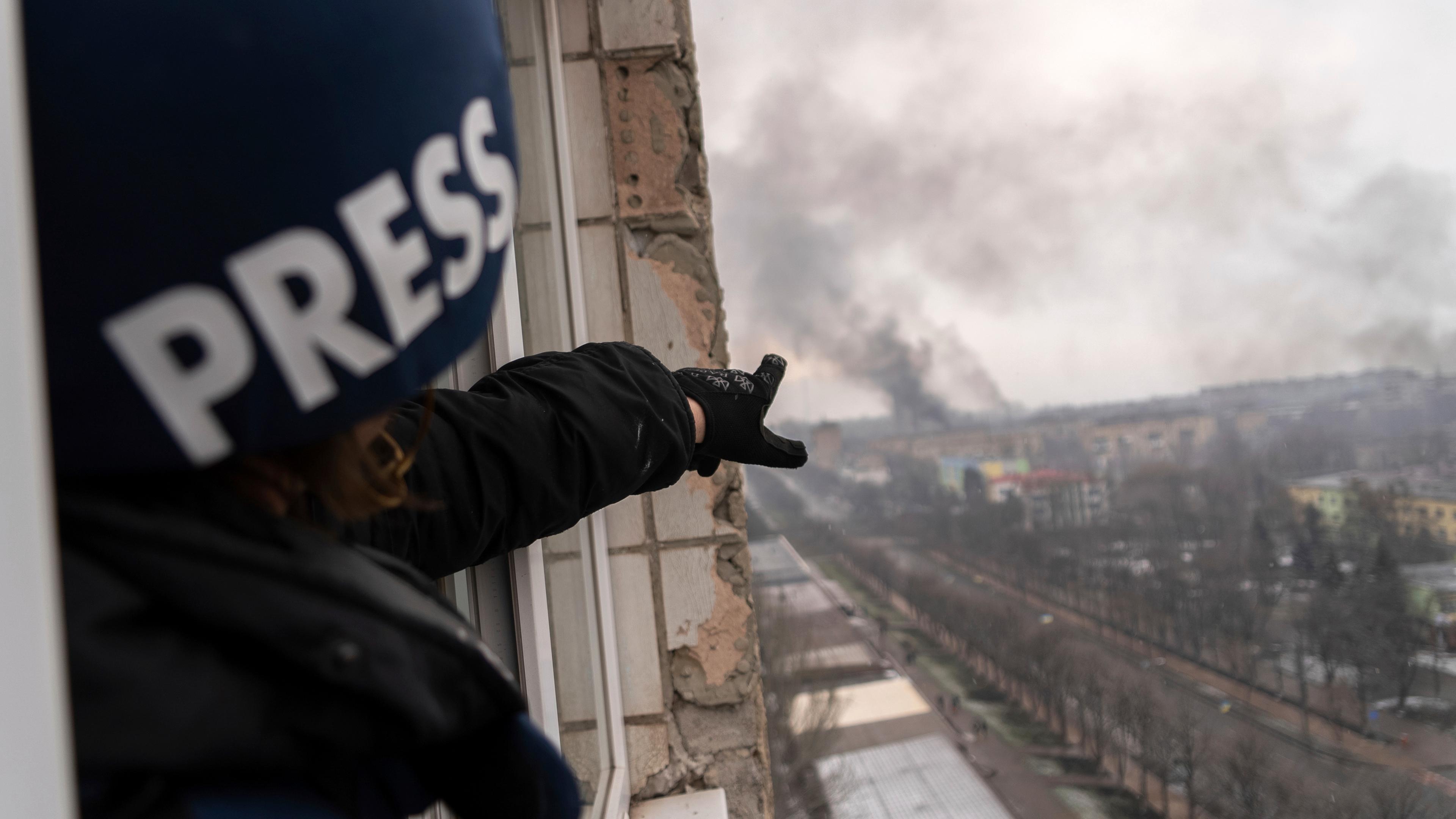 Der Fotograf Evgeniy Maloletka, der einen Helm mit der Aufschrift "Press" trägt, zeigt aus dem Fenster eines beschädigten Hochhauses auf Rauchwolken über der Stadt Mariupol.