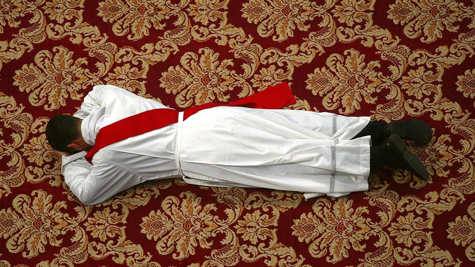 Ein junger Priester liegt betend auf dem Bauch.