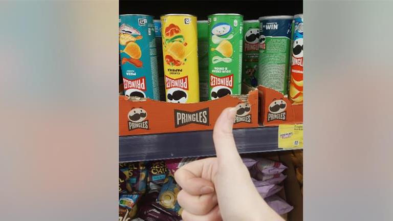 Eine Hand, die vor mehreren Pringles-Dosen den Daumen nach oben zeigt