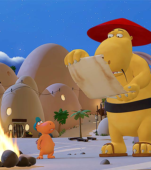 Magnus liest aus einer Papierrolle vor, während Kokosnuss und seine Freunde um ein Lagerfeuer versammelt stehen.