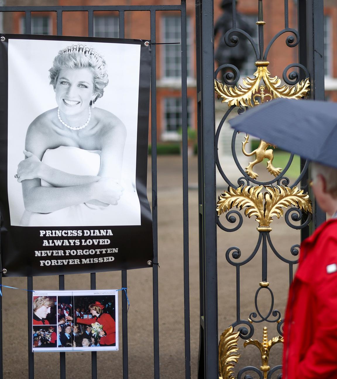 Eine Person mit Regenschirm schaut Bild Prinzessin Dianas am Kensington Palace an