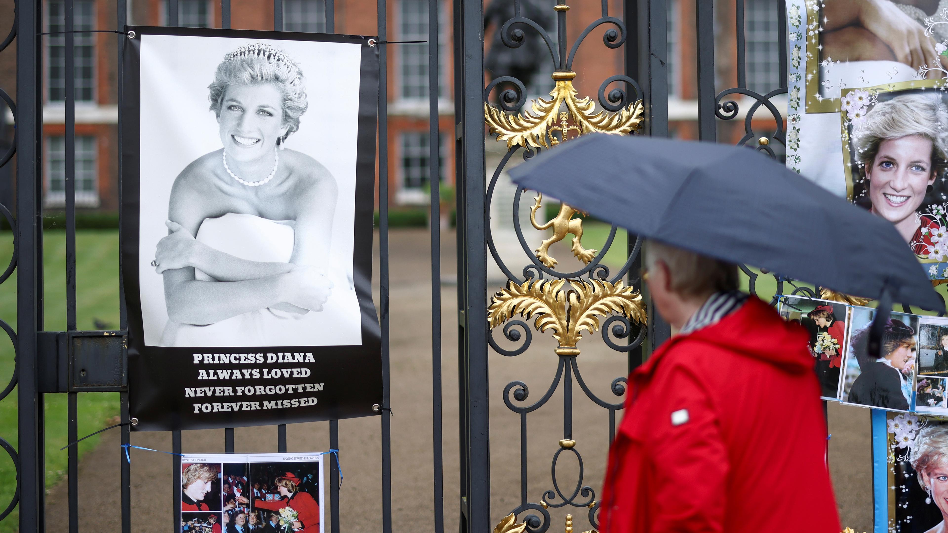 Eine Person mit Regenschirm schaut Bild Prinzessin Dianas am Kensington Palace an