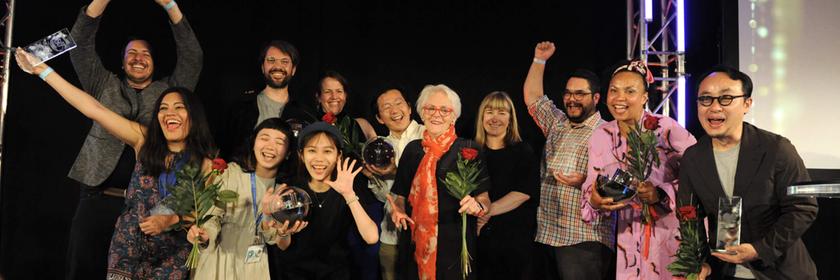 Eine Gruppe von Preisträgerinnen und Preisträgern präsentiert stolz ihre Trophäen auf der Bühne. Der Moment hält die Freude über den Gewinn des Prix Jeunesse International 2024 fest.