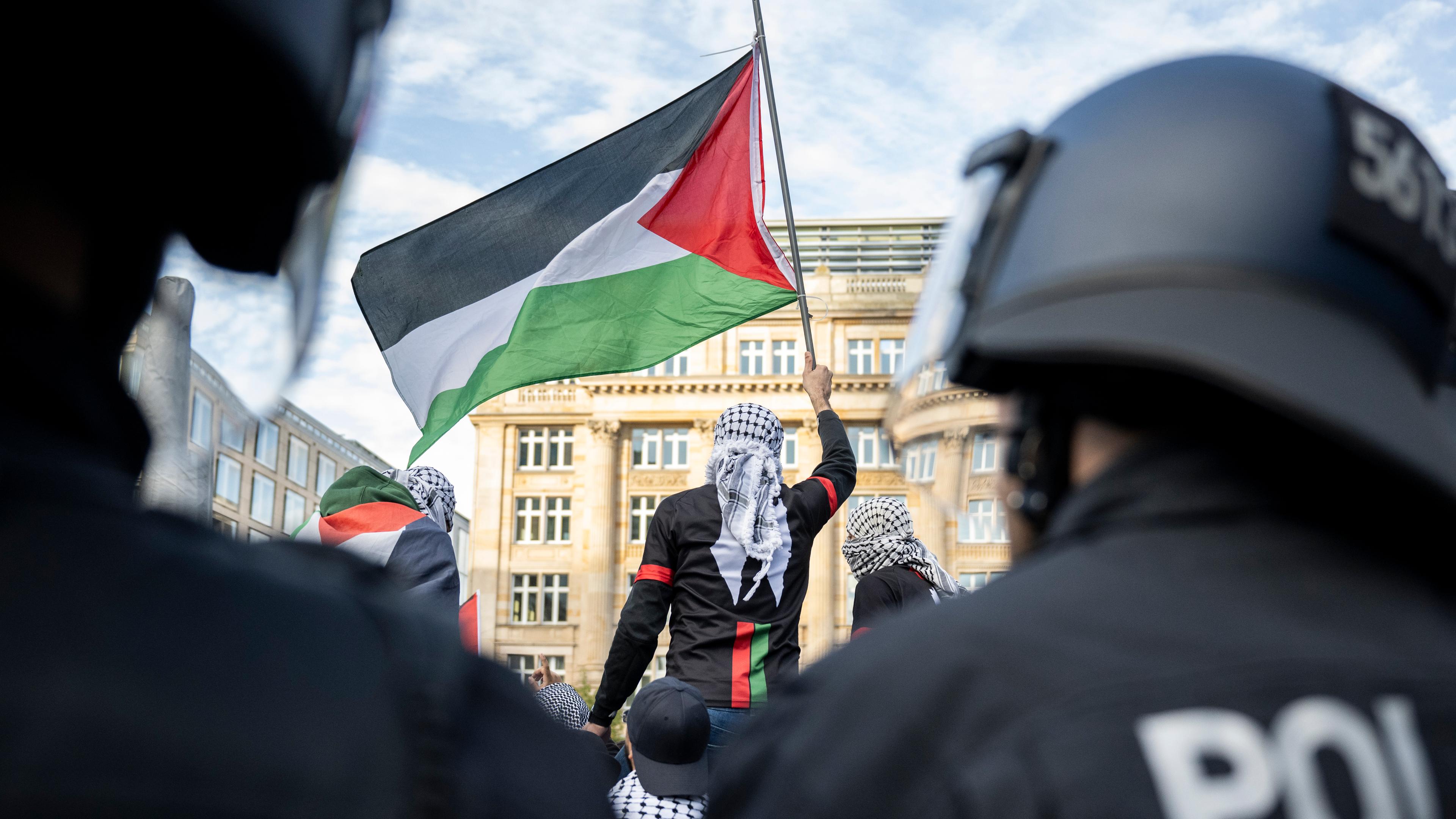14.10.2023, Hessen, Frankfurt/Main: Ein Teilnehmer einer Pro-Palästina Demonstration schwenkt eine Palästina-Flagge, während Polizisten die Situation beobachten.