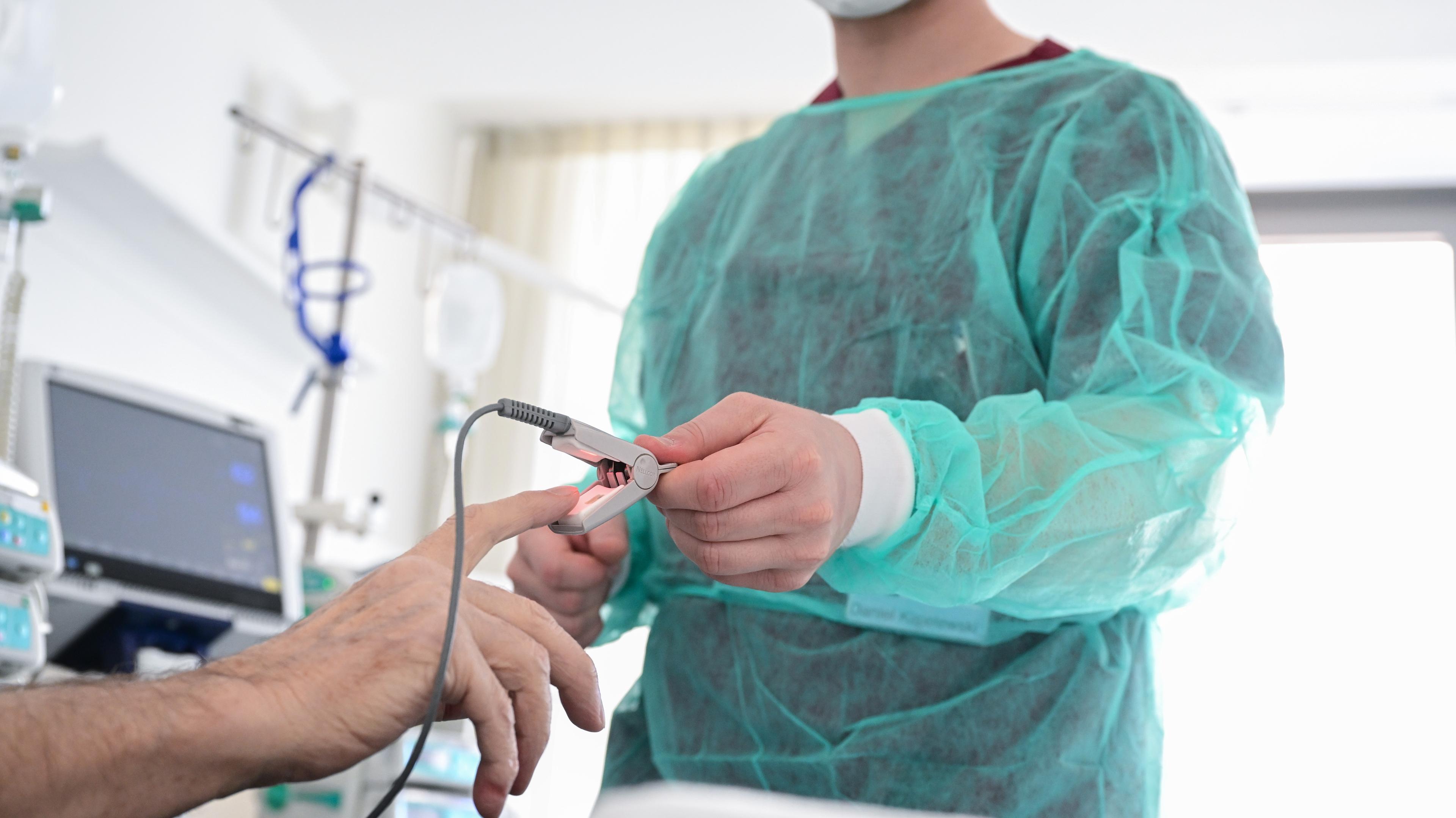 Ein Pfleger legt in einem Krankenzimmer im Klinikum Stuttgart bei einem Patienten ein Messgerät an.