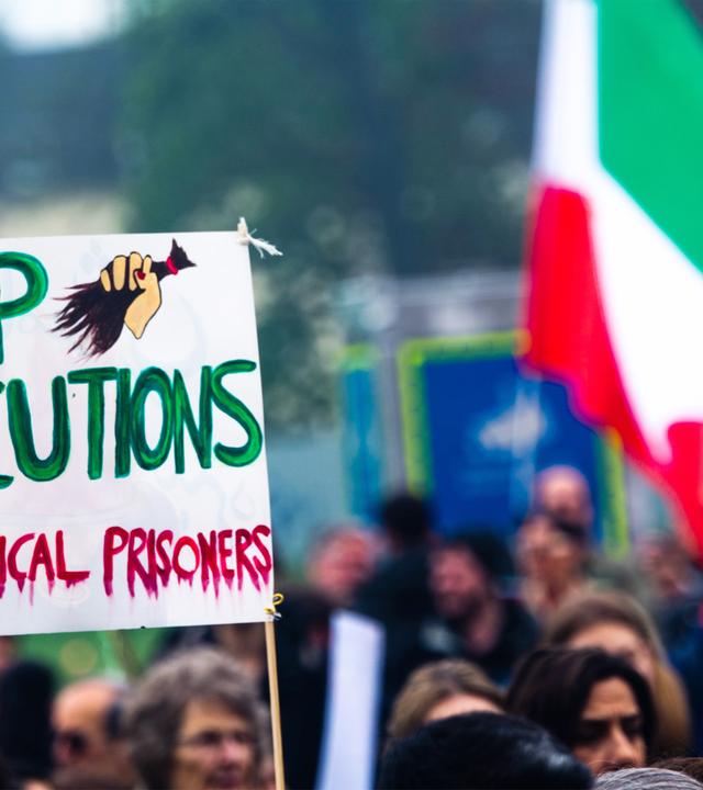 Demonstranten halten ein Schild hoch, auf dem steht stoppt Hinrichtungen, befreit politische Gefangene und tragen eine iranische Flagge.