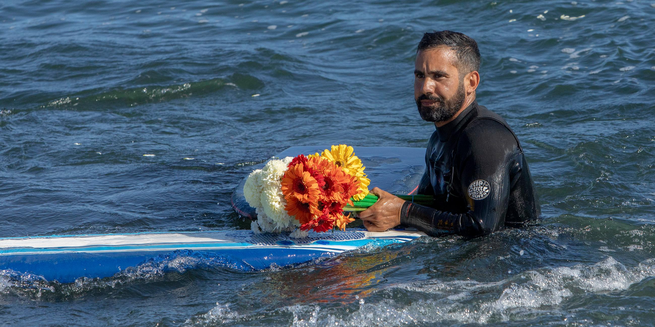 Ein Mann hält Blumen während einer Gedenkfeier für drei vermisste Surfer in Ensenada, Mexiko