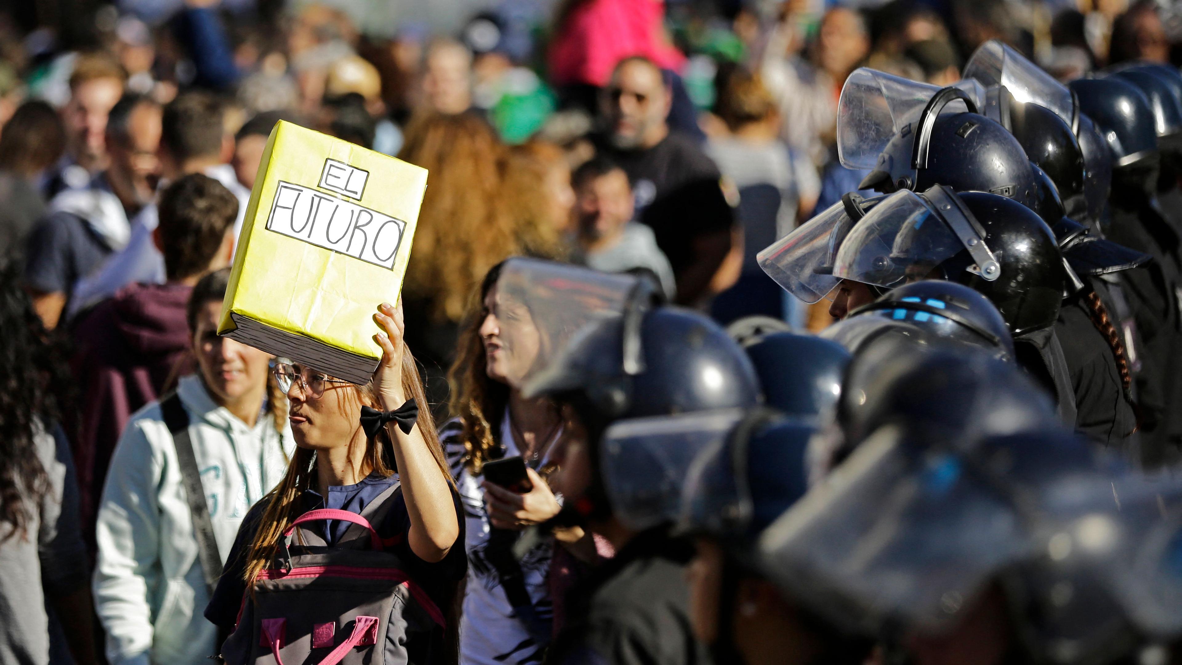 Menschen die gegen die argentinische Sparpolitik protestieren, im Vordergrund sind verschwommen Polizsten mit Helmen zu sehen