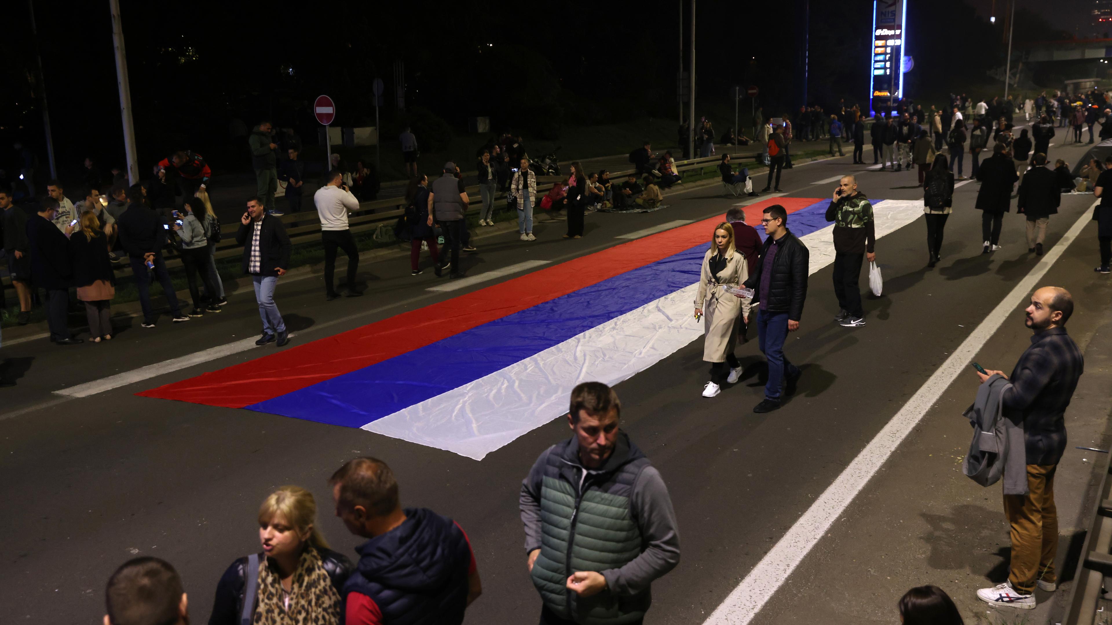Leute laufen mit einer großen serbischen Flagge einen Highway entlang.