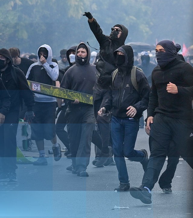 Vermumte Protestiernde und das Denkmal der Marianne mit einer gelben Weste