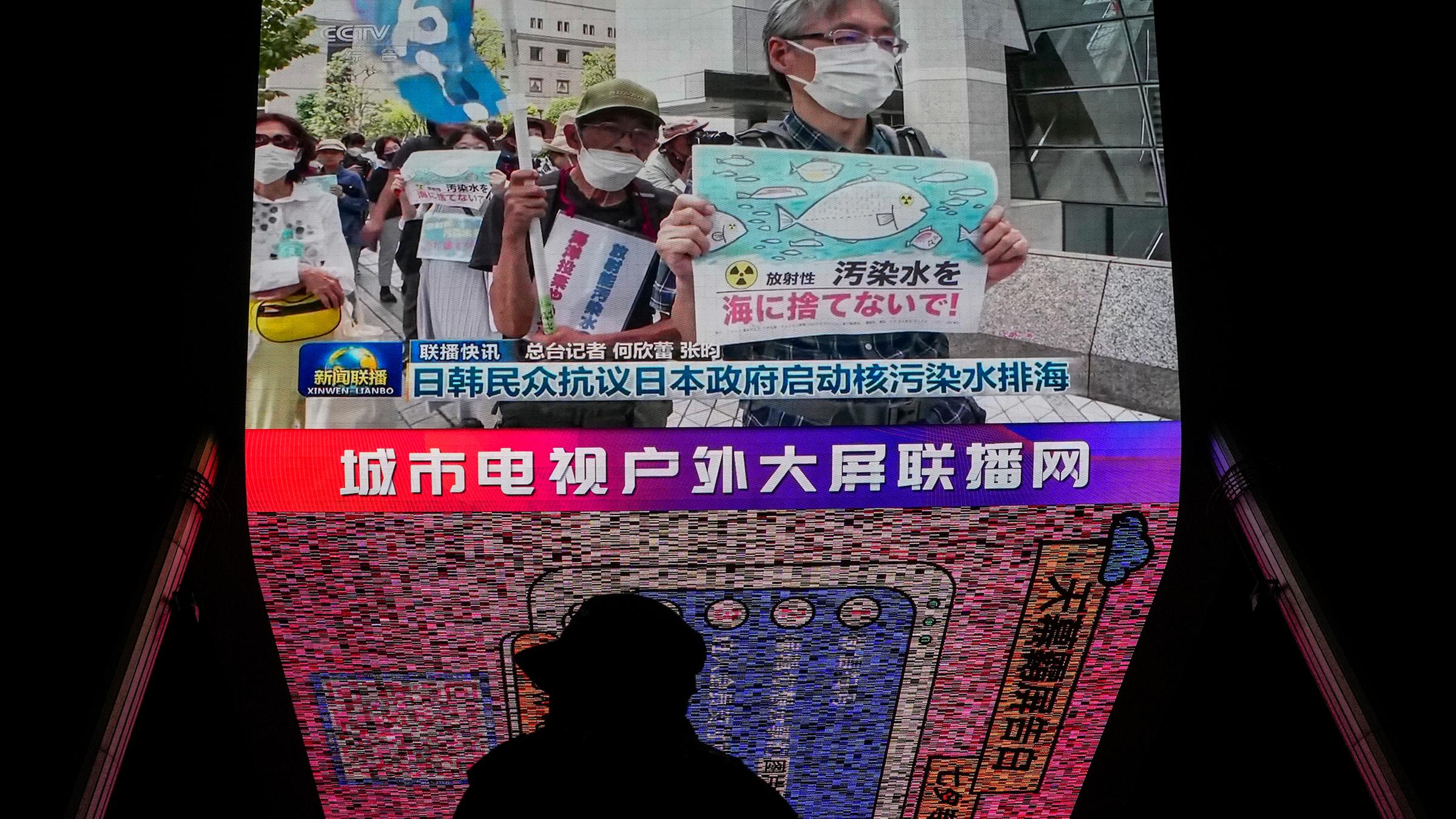 Ein Mann steht in Peking vor einem Bildschirm, auf dem Nachrichten über japanische und südkoreanische Proteste gezeigt werden am 24.08.2023.