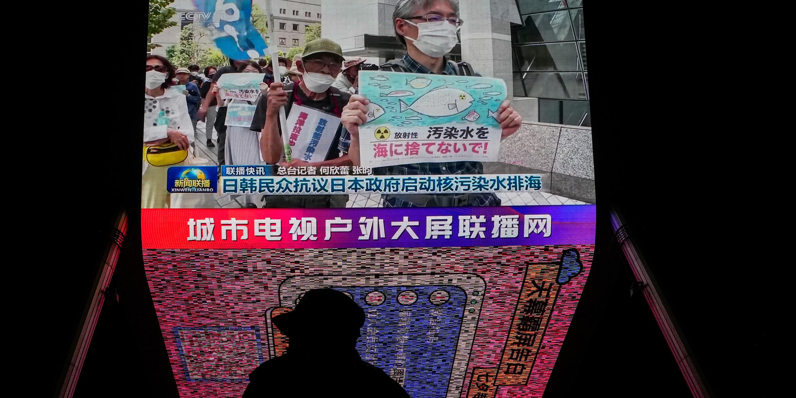Ein Mann steht in Peking vor einem Bildschirm, auf dem Nachrichten über japanische und südkoreanische Proteste gezeigt werden am 24.08.2023.