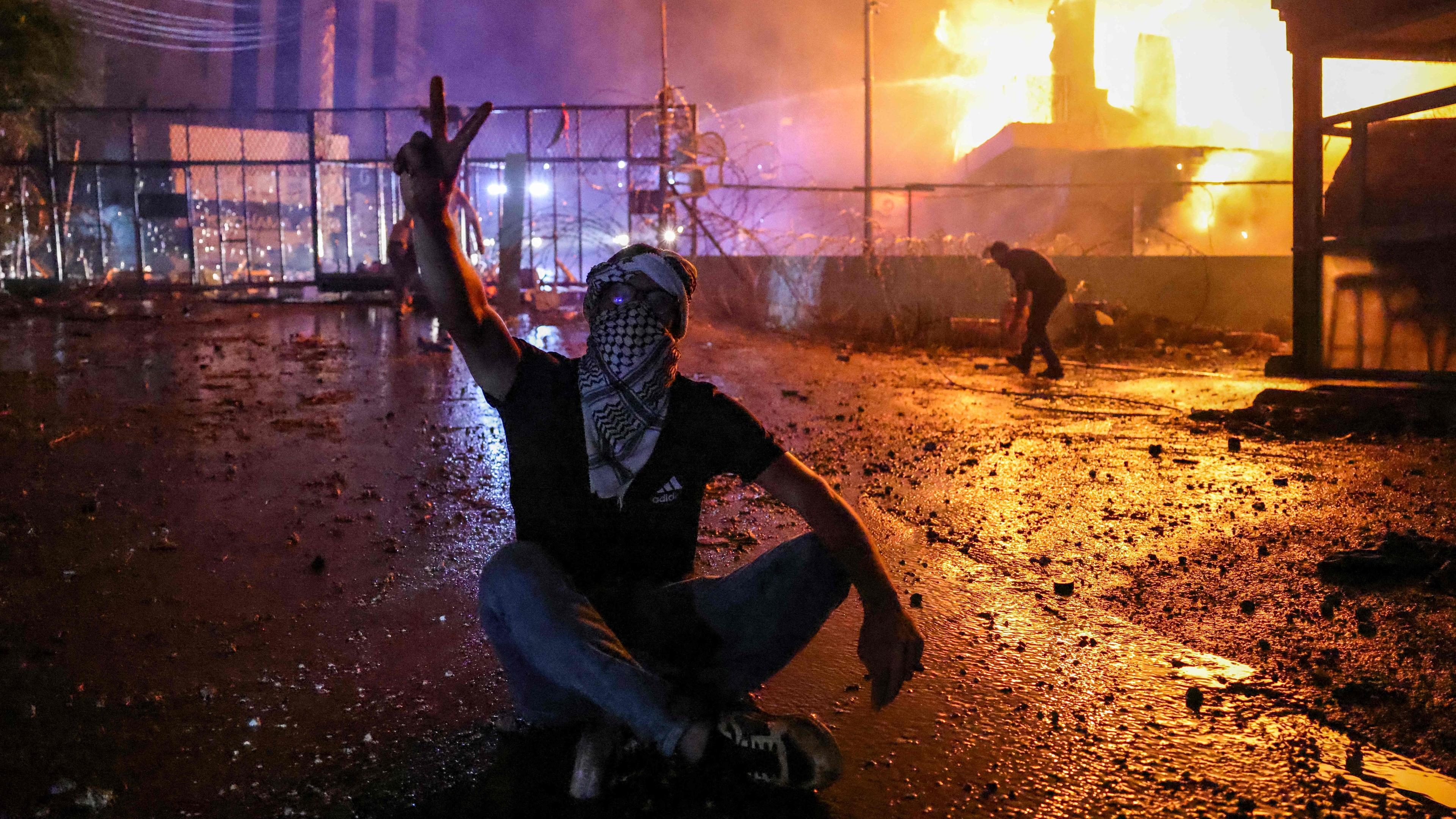 Ein Teilnehmer von Protesten im Libanon gegen israelische Angriffe auf Gaza zeigt das Victory-Handzeichen vor brennenden Barrikaden.