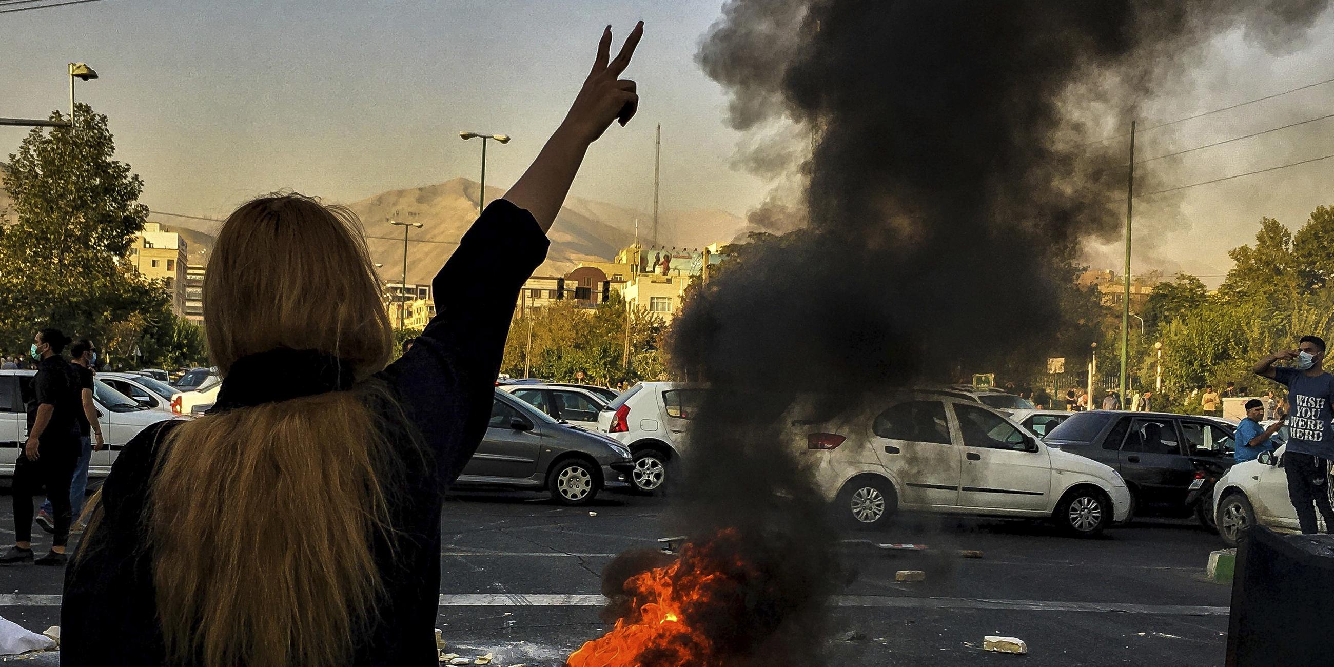 Archiv: Eine Frau steht während einer Demonstration nach dem Tod der 22-jährigen Mahsa Amini vor einem brennenden Autoreifen und zeigt das Victory-Zeichen. 