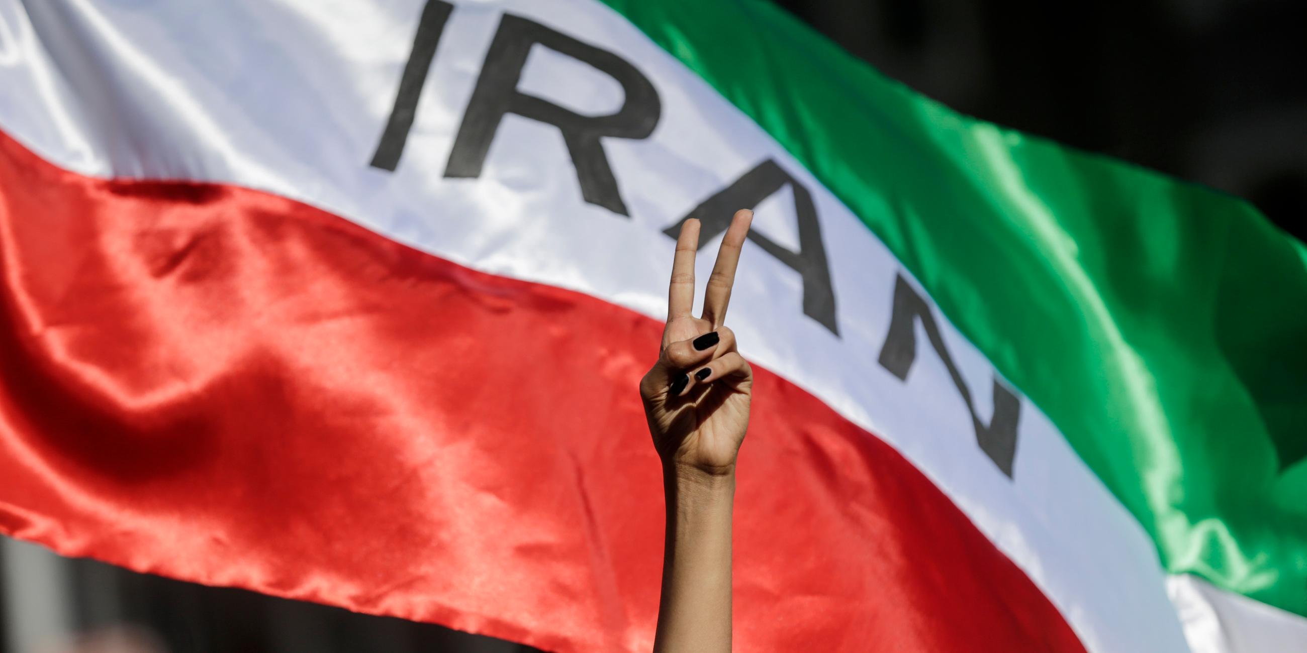 Italien, Rom: Eine Frau zeigt auf einer Demonstration iranischer Studenten für die Menschenrechte im Iran das Victory-Zeichen vor einer iranischen Fahne.