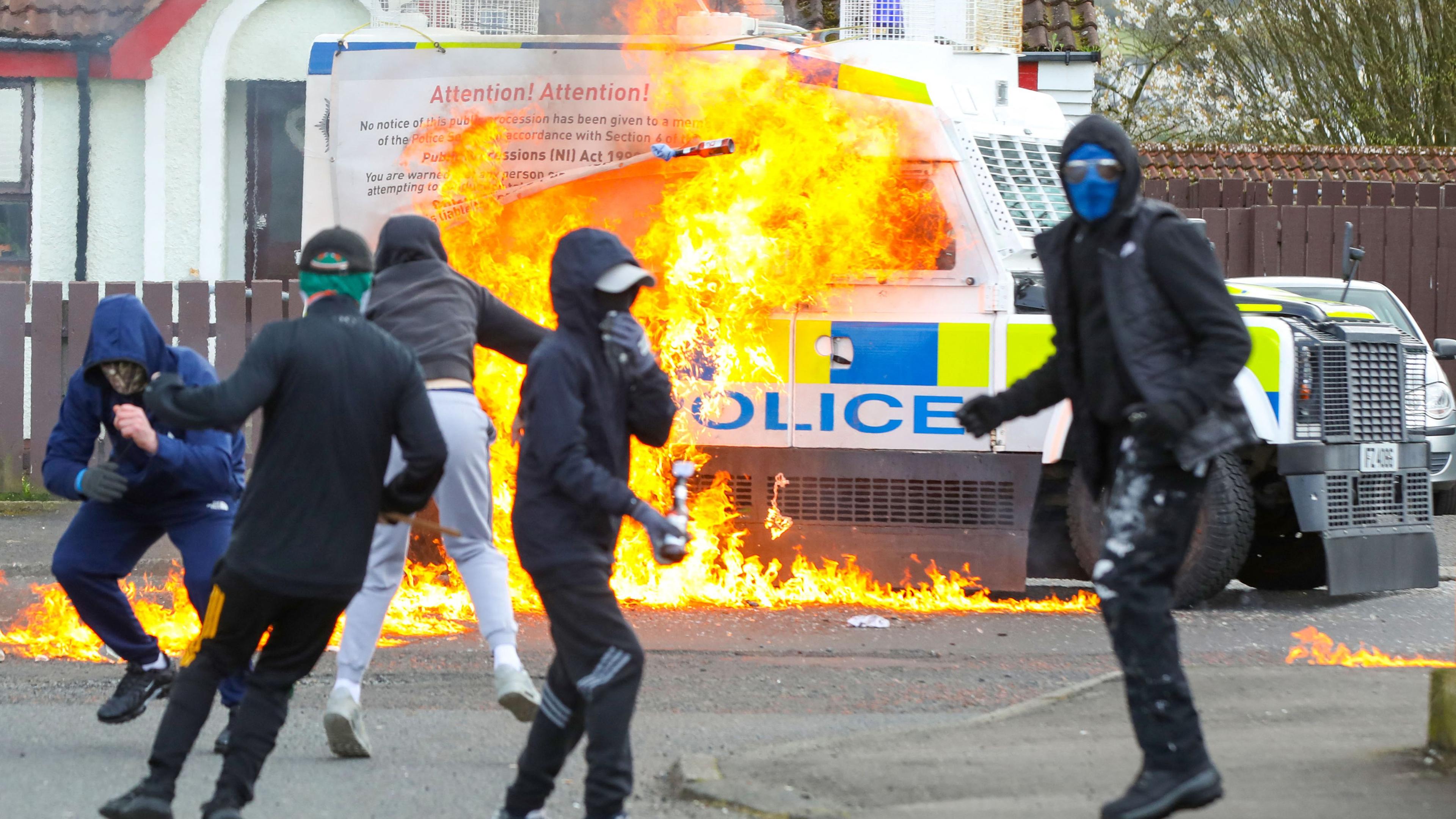 Maskierte Jugendliche setzten einen Polizeiwagen in Flammen während Protesten in Nordirland.